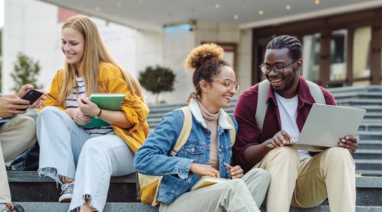 Students use their devices while sitting on the steps of a college building